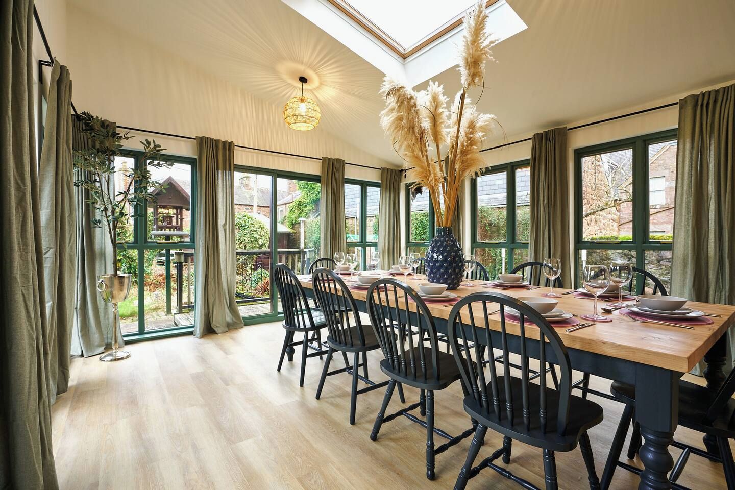 Comedor con una mesa alta dispuesta para seis personas, rodeado de sillas y vistas a la vegetación exterior a través de amplias ventanas.