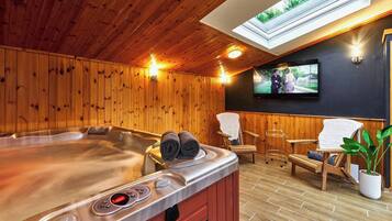 Una sala de sauna con paredes de madera, una bañera de hidromasaje y un televisor montado en la pared.