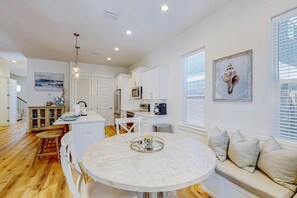 A modern kitchen with white cabinetry, a round dining table, and a built-in oven. - The Spotted Sandpiper (Miramar Beach)