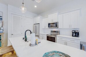 A modern kitchen with white cabinetry, stainless steel appliances, and a central island with a sink. - The Spotted Sandpiper (Miramar Beach)