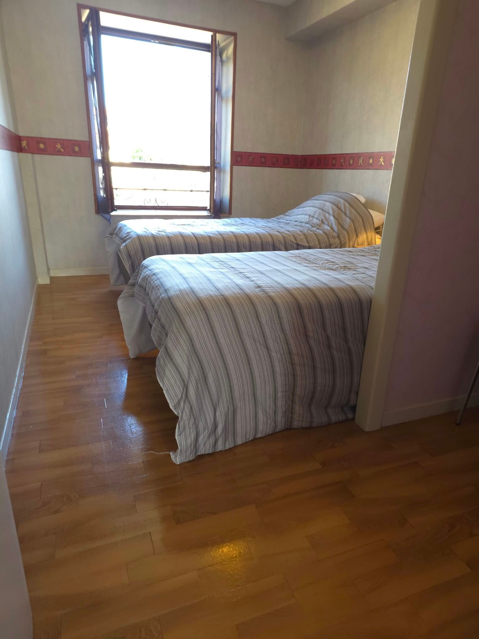 A room with two beds, wooden flooring, and a window.