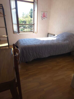 Una camera da letto con un letto, una sedia, un termosifone e una finestra vista su vegetazione.