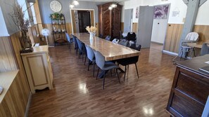 A spacious dining area with a long wooden table and chairs, a clock on the wall, and a door leading to another room.
