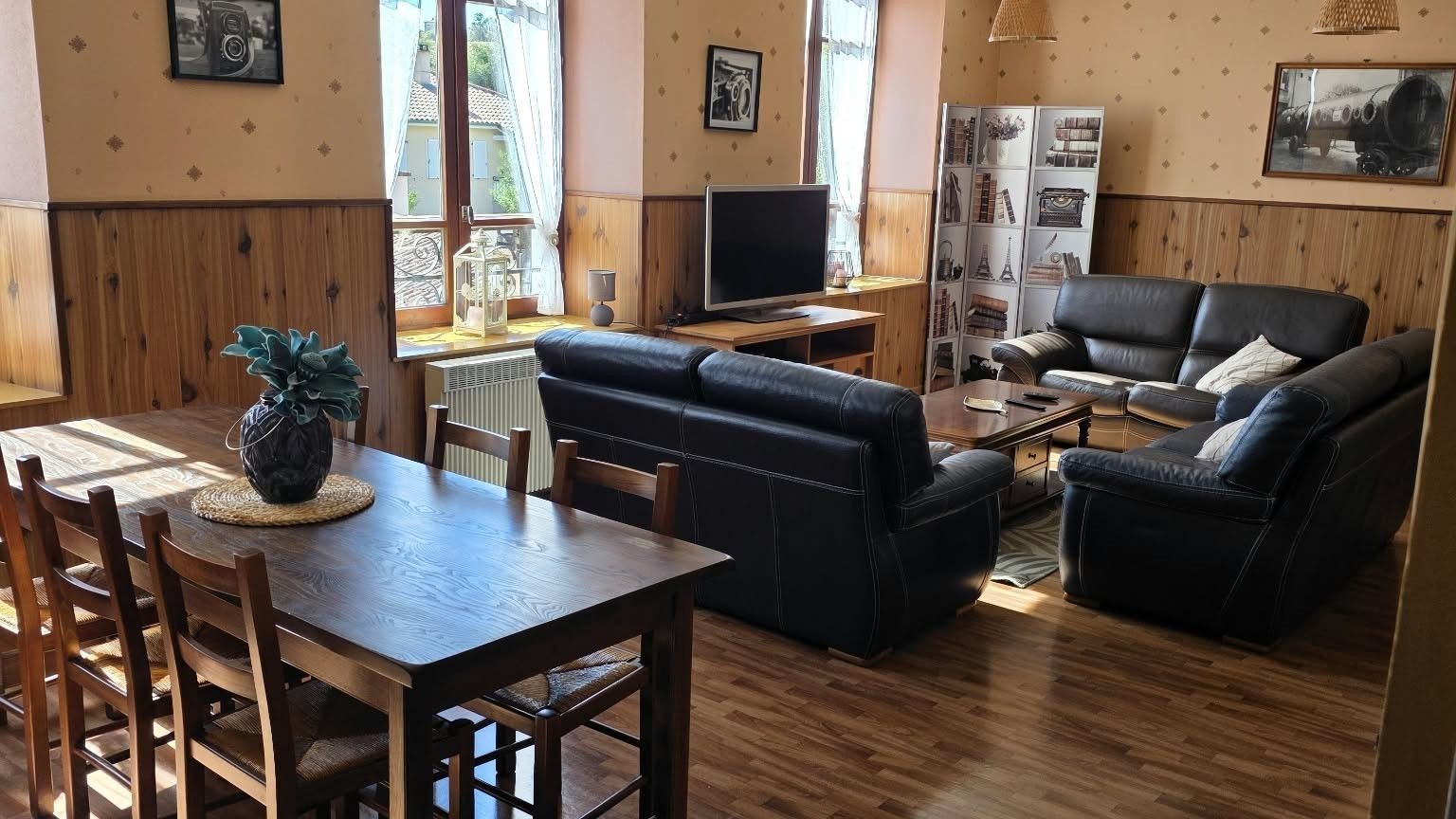 A living room with a wooden dining table, black leather sofa, and a television.