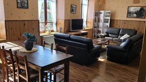 A living room with a wooden dining table, black leather sofa, and a television.