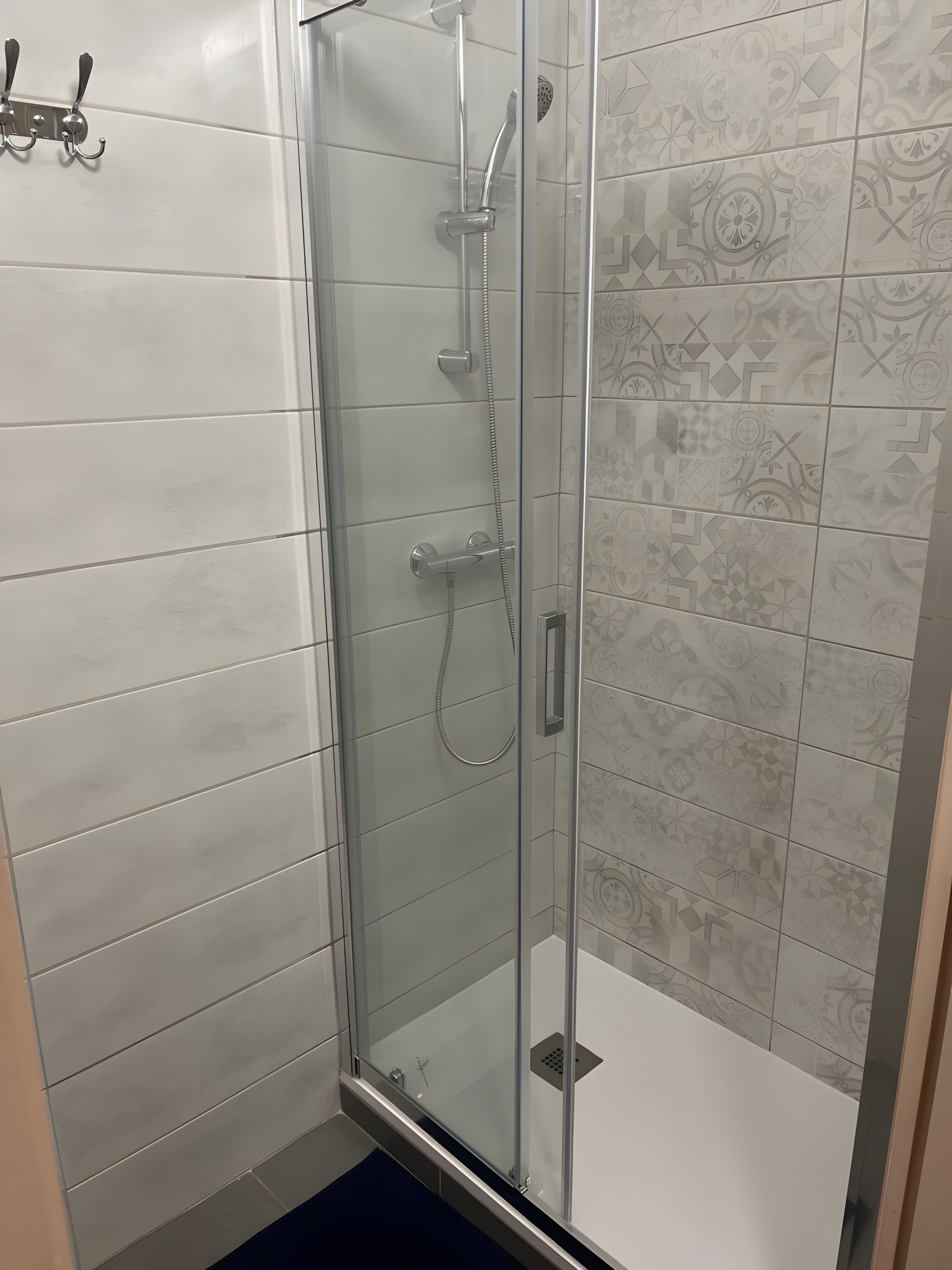 Una ducha con puerta de vidrio, un cabezal de ducha manual y un grifo empotrado en la pared.