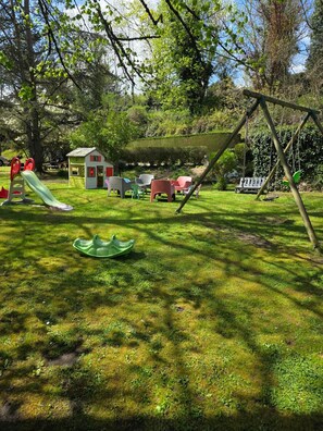 A playground with a slide, swings, and a small house.