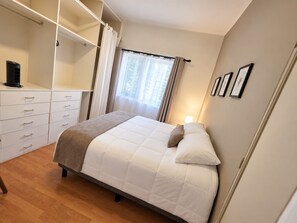 Ein Schlafzimmer mit einem Bett, einem Kleiderschrank, einem Fenster mit Vorhängen und einer Nachttischlampe.
