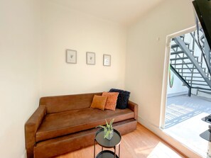 Ein Wohnzimmer mit einem braunen Sofa, einem kleinen runden Tisch mit einer Pflanze und drei gerahmten Bildern an der Wand.