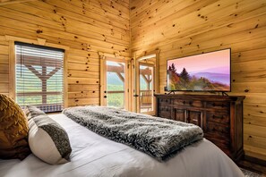 Ein Schlafzimmer in einer Holzhütte mit einem Bett, einem Fernseher und Blick ins Freie.