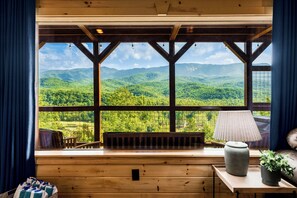 Eine Holzblockhütte mit einem großen Fenster mit Blick auf eine bewaldete Bergkette.