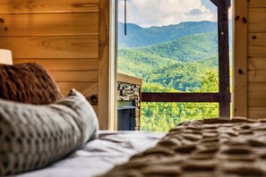 A bedroom with a view of a forested mountain range through a window. - Mtn & Golf Views 3King Suites Theater GmRm HotTub (Gatlinburg)