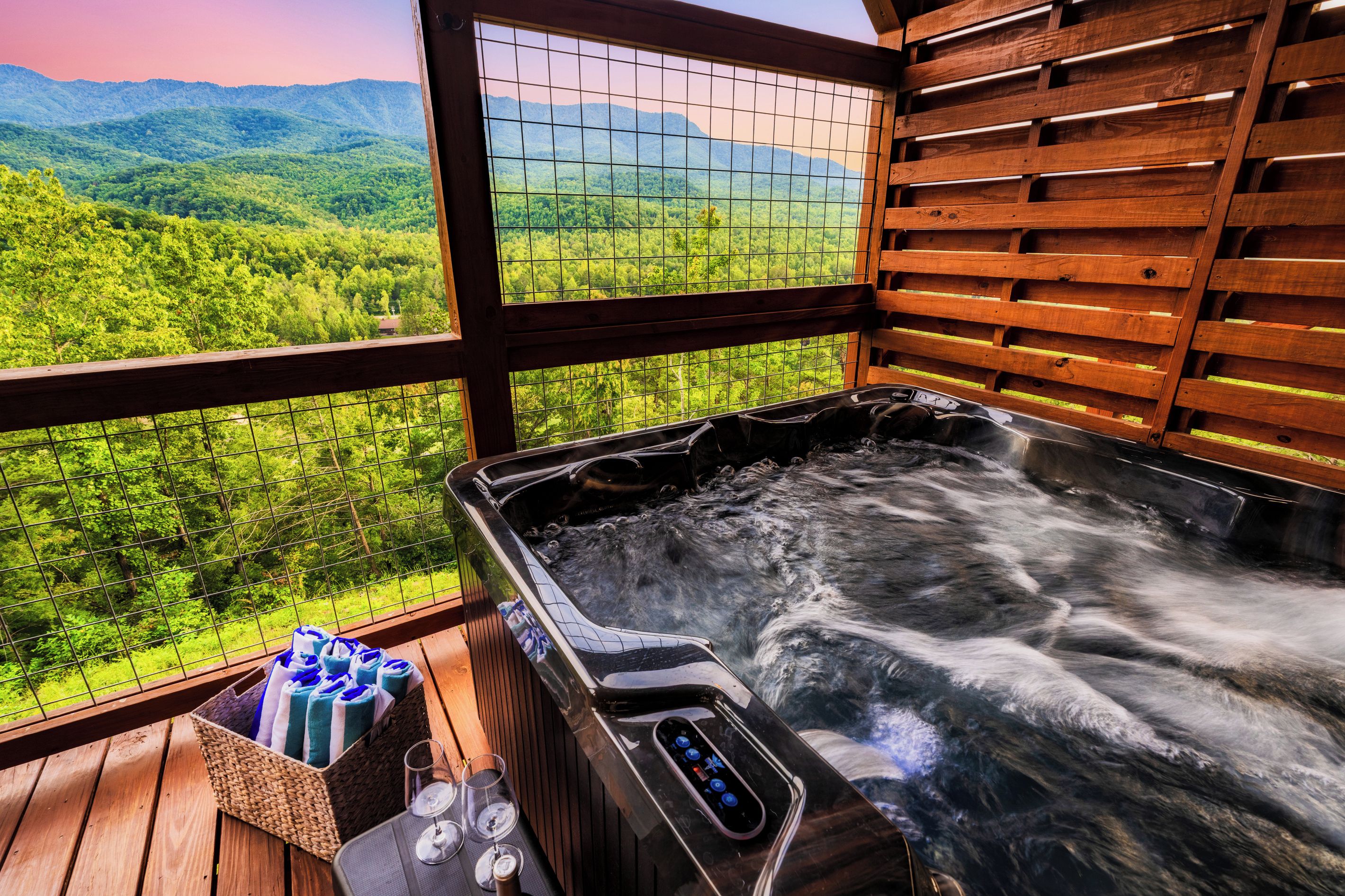 A hot tub with a wooden deck and a view of a forested mountain range.