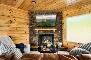 A cozy room with a stone fireplace, a television mounted on the wall, and a comfortable seating area with a coffee table. - Mtn & Golf Views 3King Suites Theater GmRm HotTub (Gatlinburg)