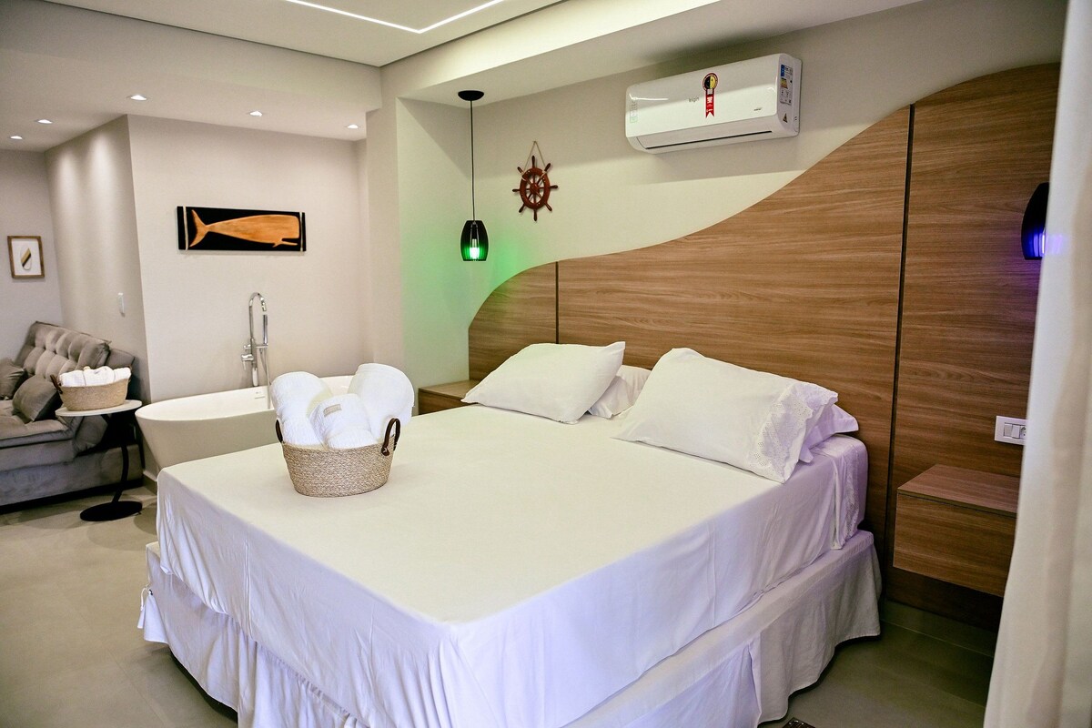 Una habitación de hotel con una cama, una mesita con una cesta, un aire acondicionado de pared, una lámpara de pared y un adorno de timón de barco en la pared.