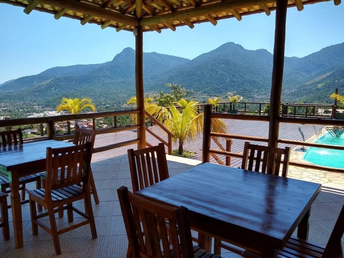 An outdoor dining area with wooden tables and chairs, a pool, and a view of mountains.