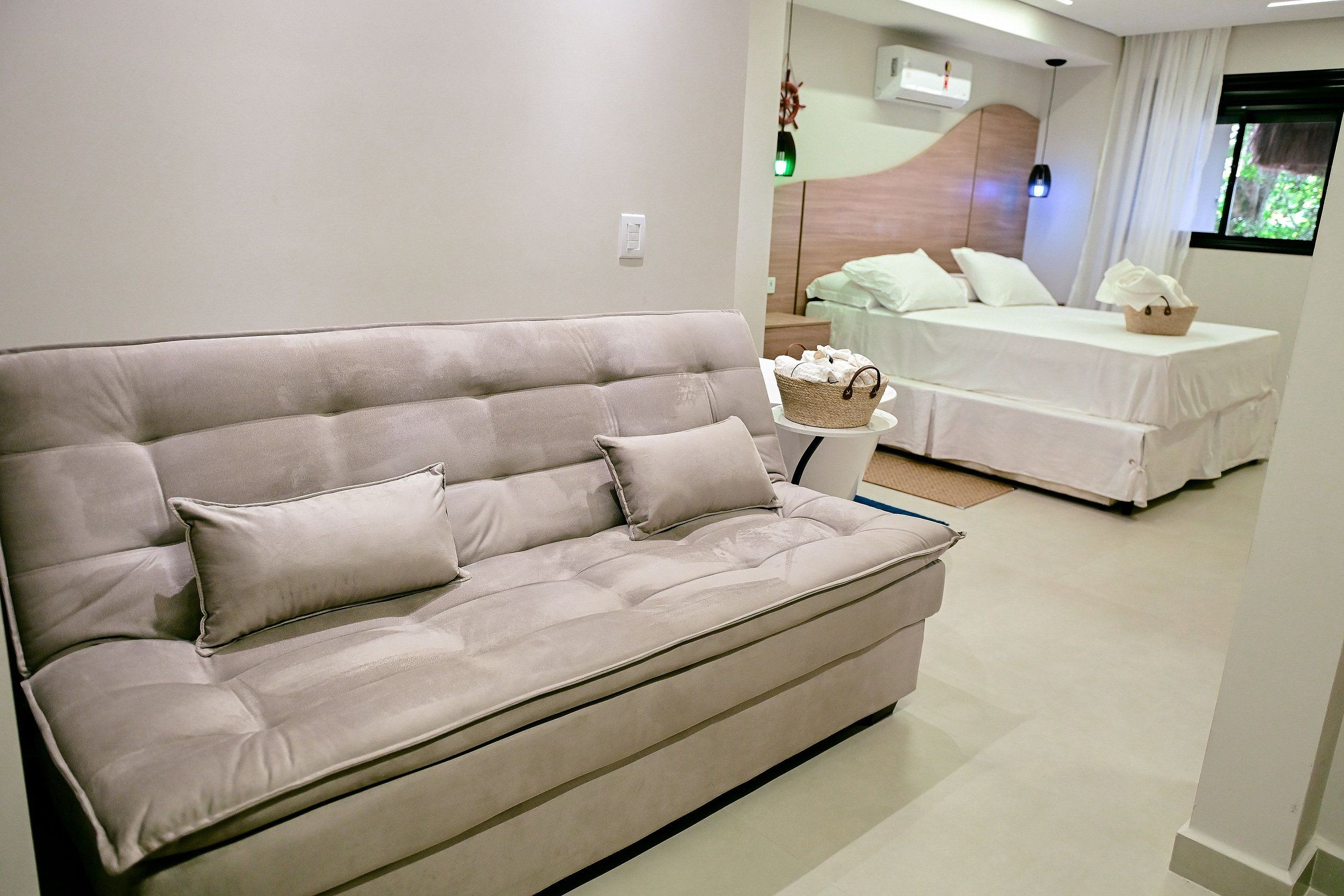 A modern living room with a beige sofa, a white bed, and a small side table with a basket.