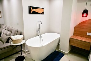 Un baño moderno con una bañera independiente, una mesita con una cesta y un banco de madera.
