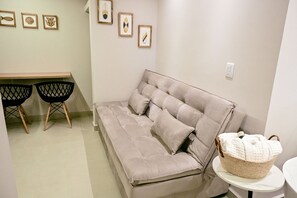 Una habitación con un sofá color beige, dos sillas negras, una mesita y una pared decorada con obras enmarcadas.