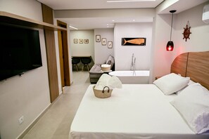 A hotel room with a bed, a TV, a bathroom with a bathtub, and a wall-mounted heater. - Studios Ilhabela (Ilhabela)