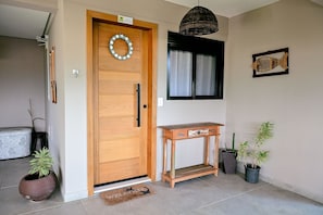 Una puerta de madera con una placa, una lámpara colgante de mimbre, una mesita de madera y plantas en macetas.