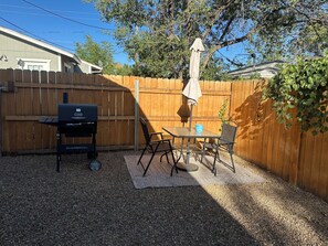 Um quintal com churrasqueira, mesa e cadeiras, e um guarda-sol.