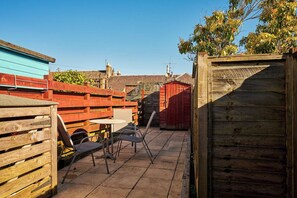 Un espace patio avec une table et des chaises, une clôture en bois et un abri de jardin rouge.