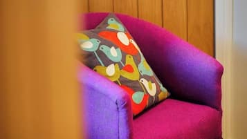 Un fauteuil violet agrémenté d’un coussin aux motifs colorés représentant des oiseaux, placé devant une porte en bois.