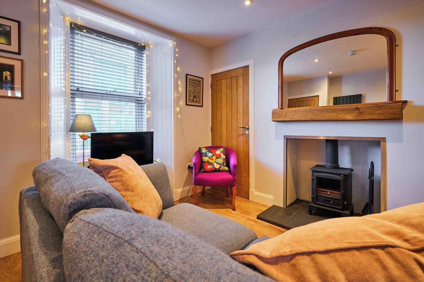 Una sala de estar acogedora con un sofá, una silla, un televisor, una chimenea y un espejo.