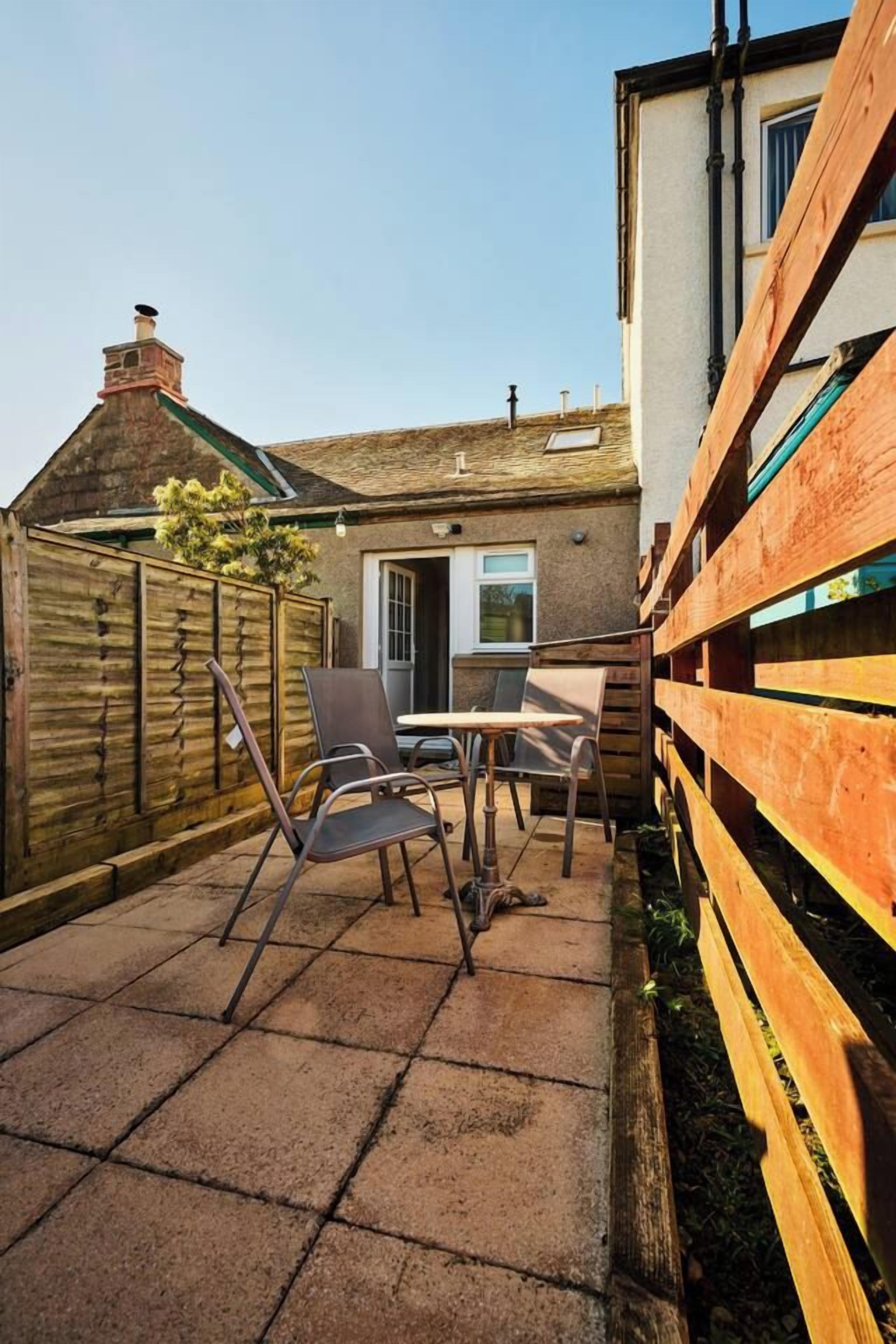 A patio with a table and chairs, a wooden fence, and a building with a door and windows.