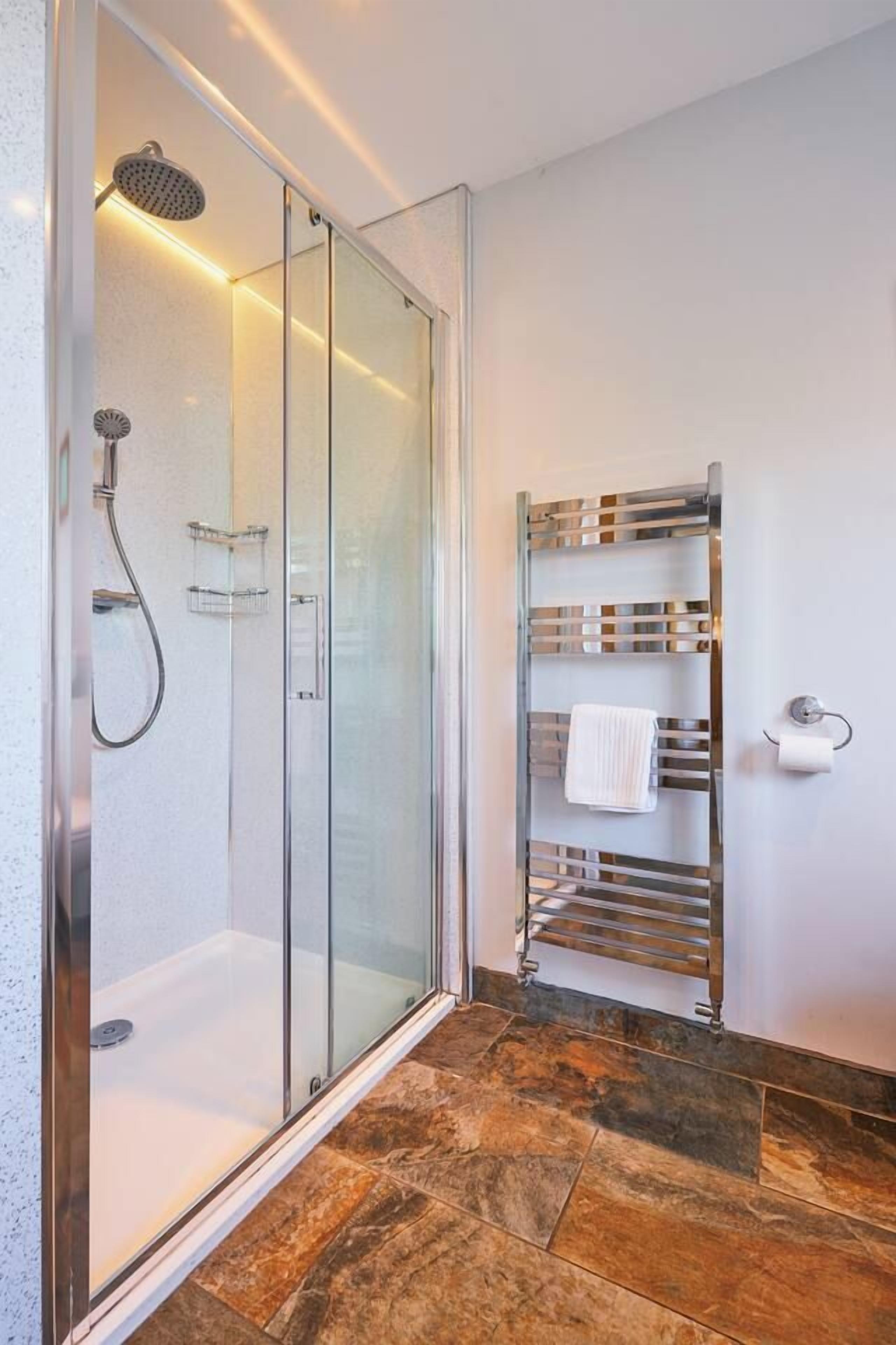 Um banheiro moderno com chuveiro em box de vidro, porta-toalhas de metal e piso revestido de azulejos.