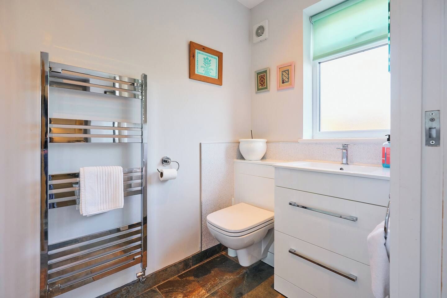 Un baño con inodoro blanco, toallero, lavamanos y ventana.