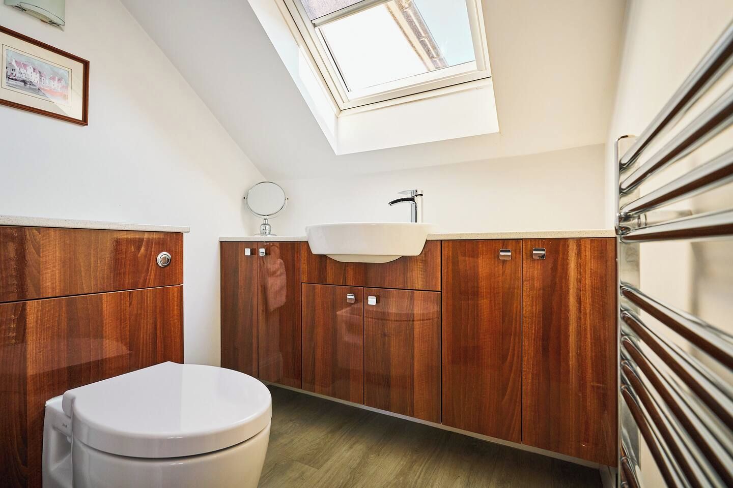 Une salle de bain moderne avec un puits de lumière, des meubles en bois, des toilettes blanches et un miroir rond.