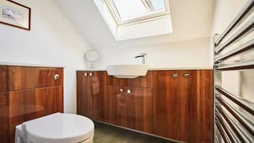 Une salle de bain moderne avec un puits de lumière, des meubles en bois, des toilettes blanches et un miroir rond.
