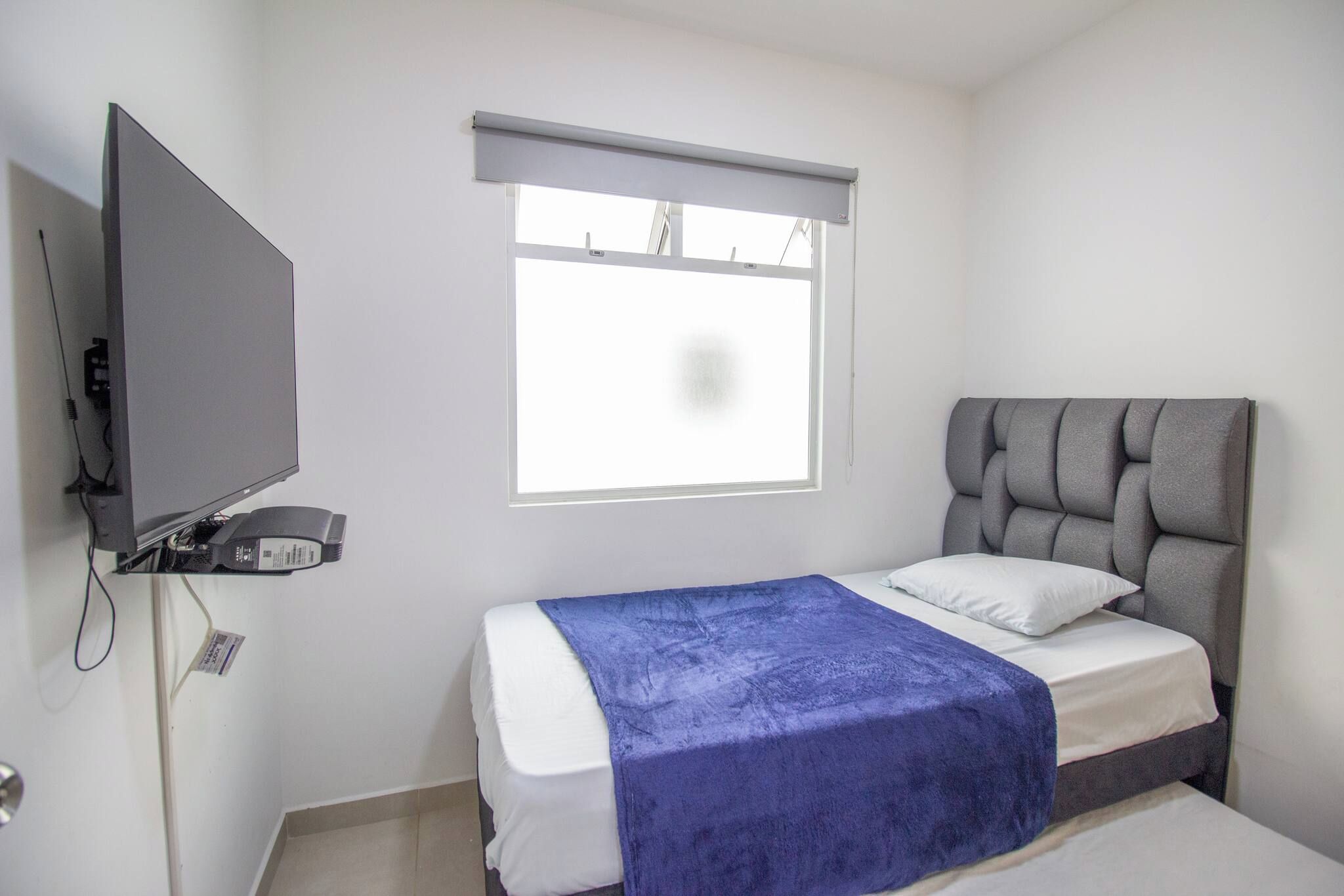 Un dormitorio con cama, televisor y ventana.