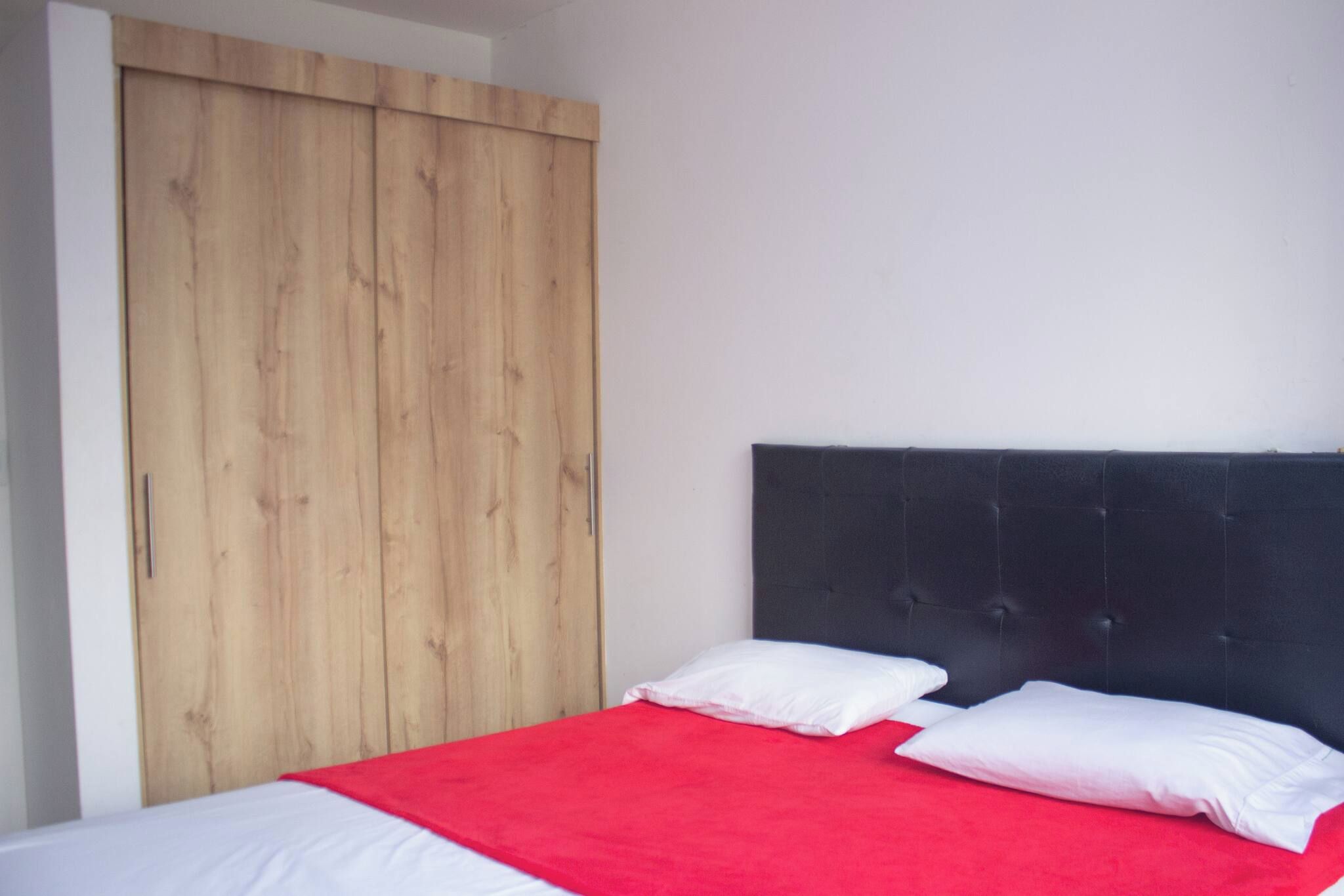 Un dormitorio con un armario de madera, una cama con cabecero negro y una colcha roja.