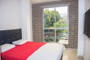 Habitación de hotel con una cama, un ventanal grande y una pared de ladrillo.