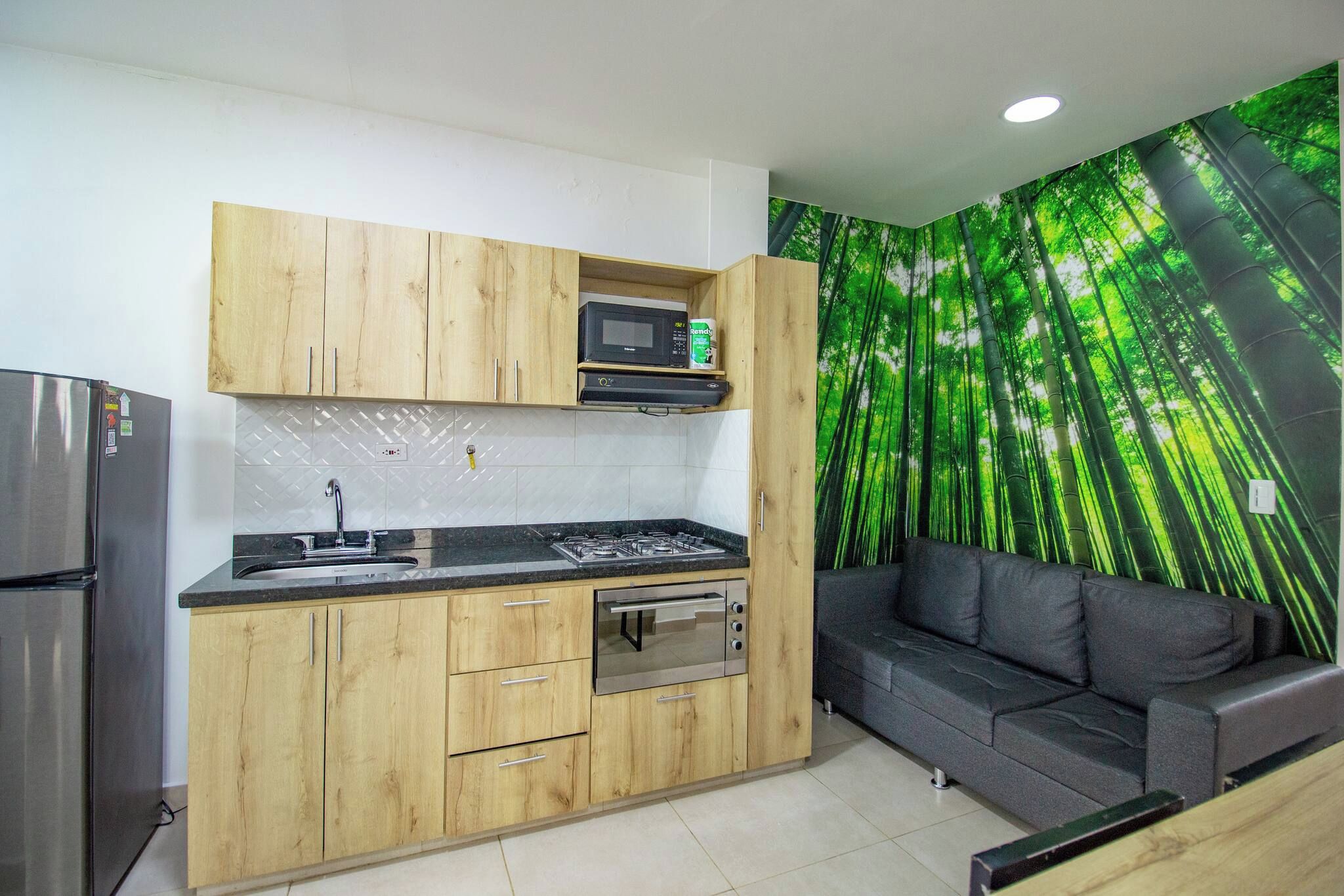 Cocina compacta con armarios de madera, microondas integrado, estufa a gas y refrigerador de acero inoxidable.