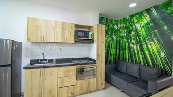Cocina compacta con armarios de madera, microondas integrado, estufa a gas y refrigerador de acero inoxidable.