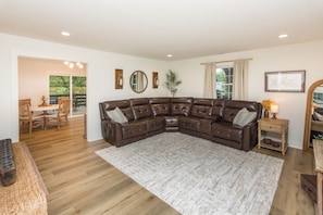 A spacious living room with a large sectional sofa, a dining area with wooden furniture, and a view of greenery through the windows. - The Julia House - Peaceful, Cozy Getaway Near Downtown Franklin (Franklin)