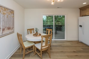 A modern kitchen with a round dining table, wooden chairs, a refrigerator, and a sliding glass door leading to an outdoor deck. - The Julia House - Peaceful, Cozy Getaway Near Downtown Franklin (Franklin)