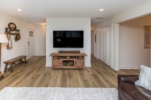 A living room with a flat-screen TV mounted on a wall, a wooden bench, a white rug, and a brown leather couch. - The Julia House - Peaceful, Cozy Getaway Near Downtown Franklin (Franklin)