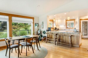 A modern kitchen with a central island, wooden cabinetry, and a dining area with a table and chairs. - Sundown Cliffs- Premium Coastal Getaway with Breathtaking Ocean Views & Sunsets (Cloverdale)