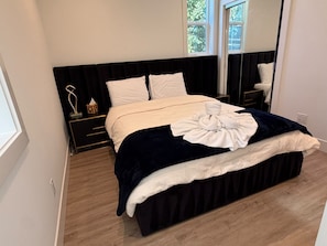 A neatly made bed with a white duvet and a dark blue blanket, a bedside table with a lamp, and a window with a view of trees. - Contemporary Modern Seattle Home (Seattle)