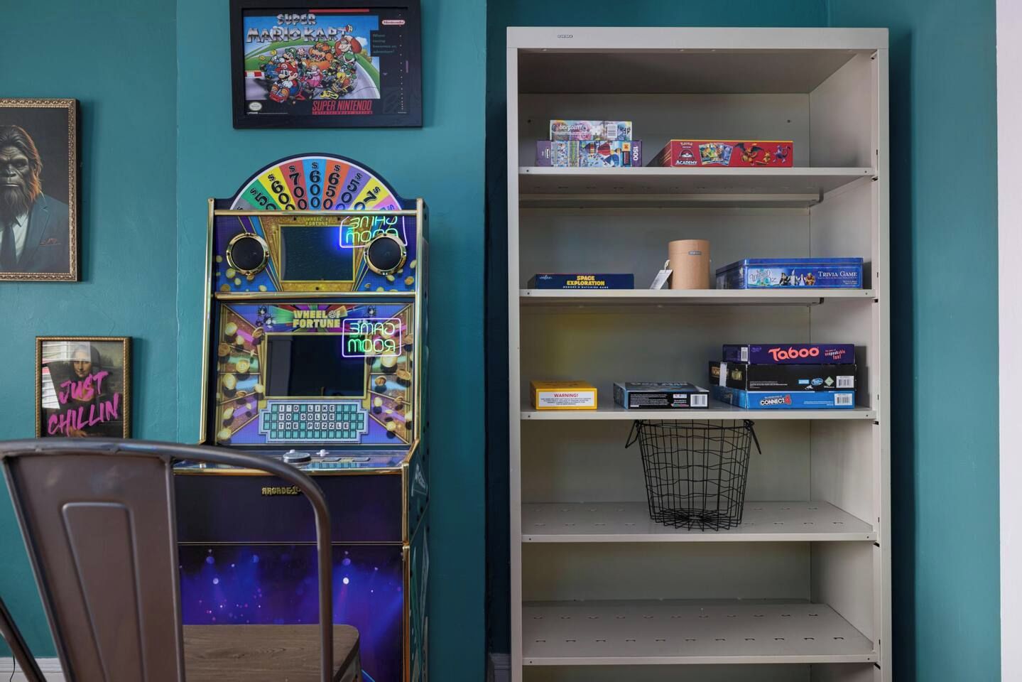 A room with a vintage arcade machine, a shelf with board games, and a framed picture on the wall.