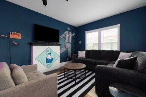 Una sala de estar con una pared azul oscuro, una chimenea, un sofá, una mesa de centro y un televisor montado en la pared.
