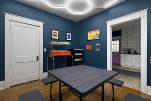 Una habitación con mesa y sillas, una kitchenette y una puerta que da a otra habitación.
