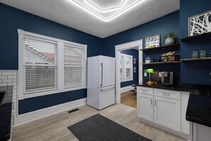 A kitchen with white cabinets, a refrigerator, a coffee maker, and a black countertop. - Jailhouse Rock Retreat {Arcade+Secret Passage} (Elizabethton)