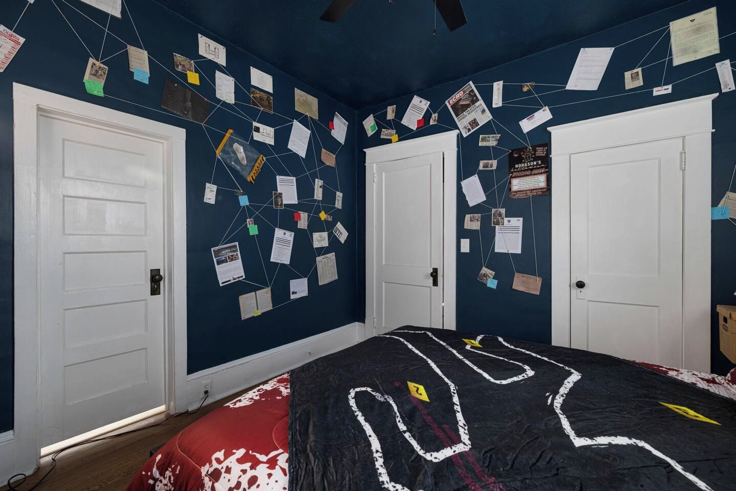 A bedroom with a bed, two white doors, and walls covered with various papers and notes.