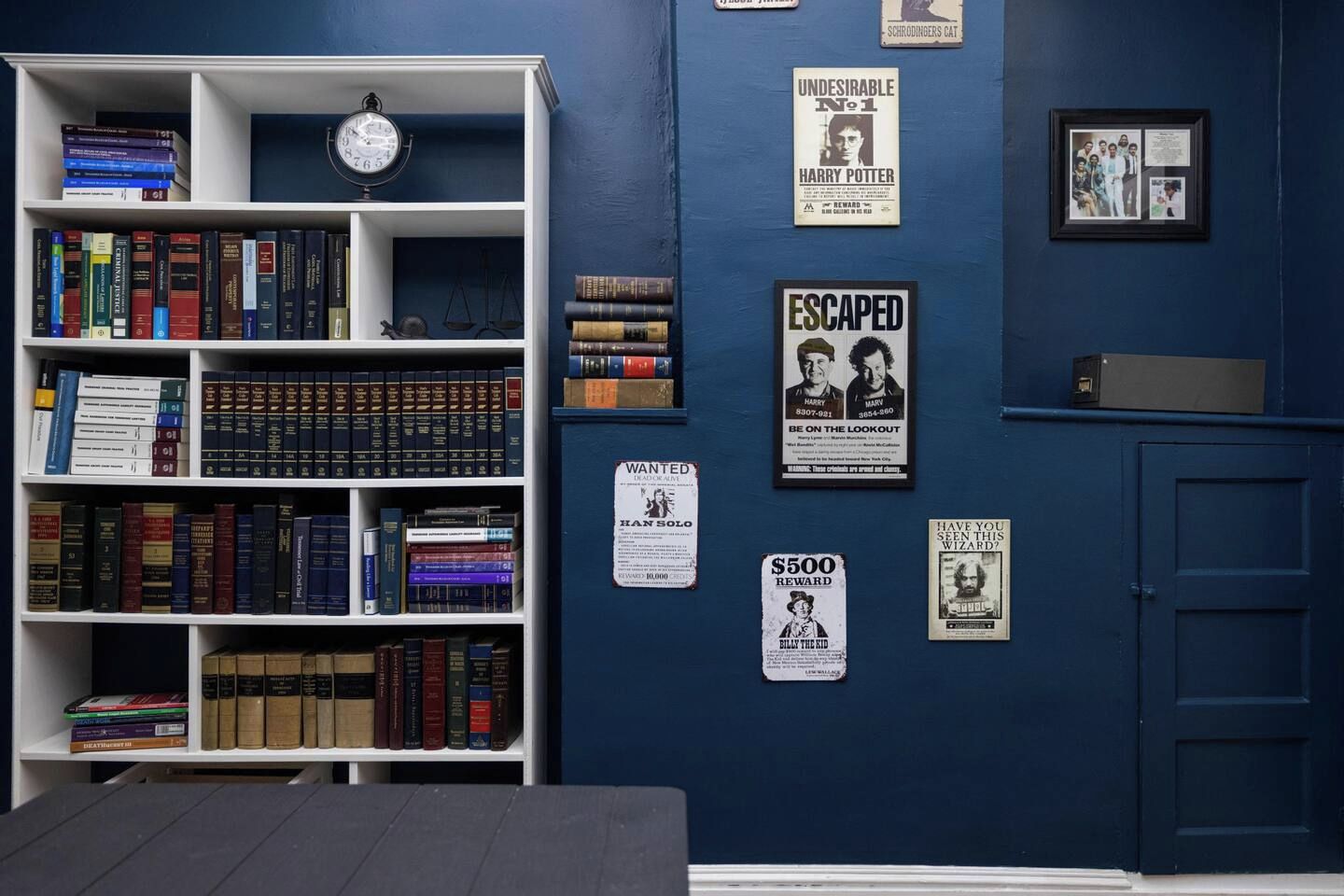A room with a bookshelf filled with books, a clock, and various posters on the wall.